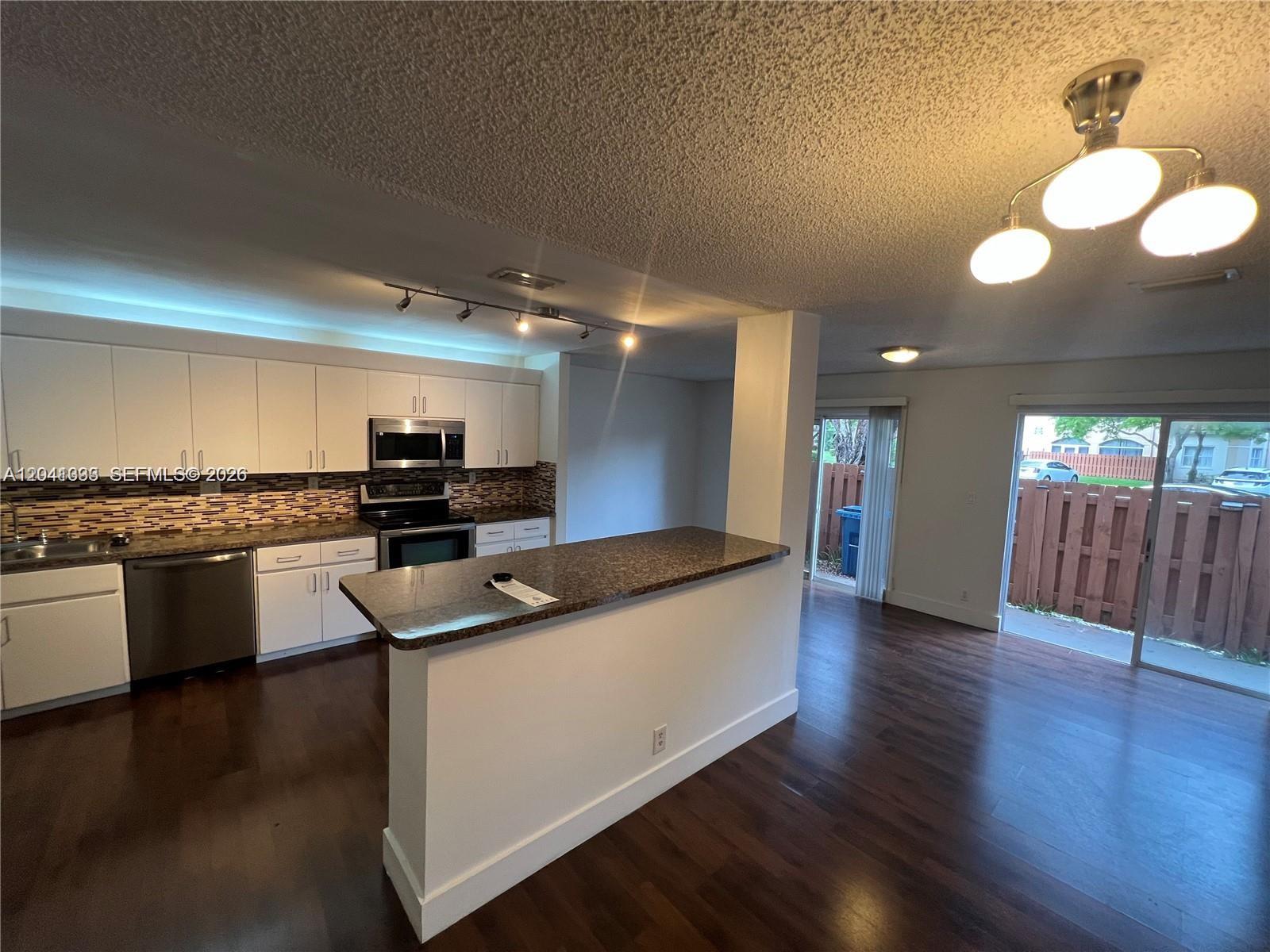 A kitchen with white cabinets and a breakfast bar opens to a living area — 561 Racquet Club Rd # 21, Weston FL 33326, WESTON, FL