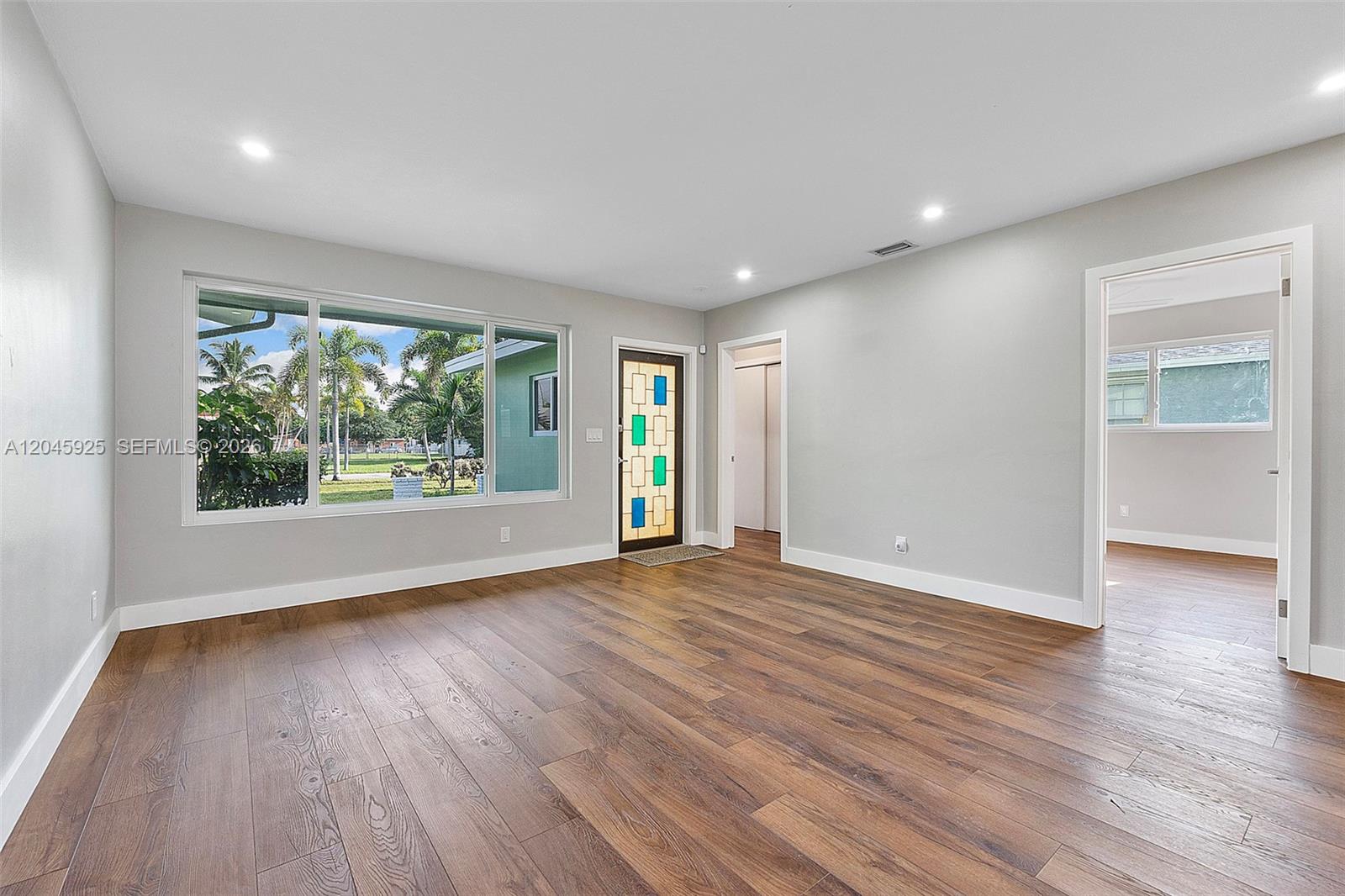 A living room features light gray walls, wood-look flooring, a large window, and a decorative door — 2230 Atlanta St, Hollywood FL 33020, HOLLYWOOD, FL