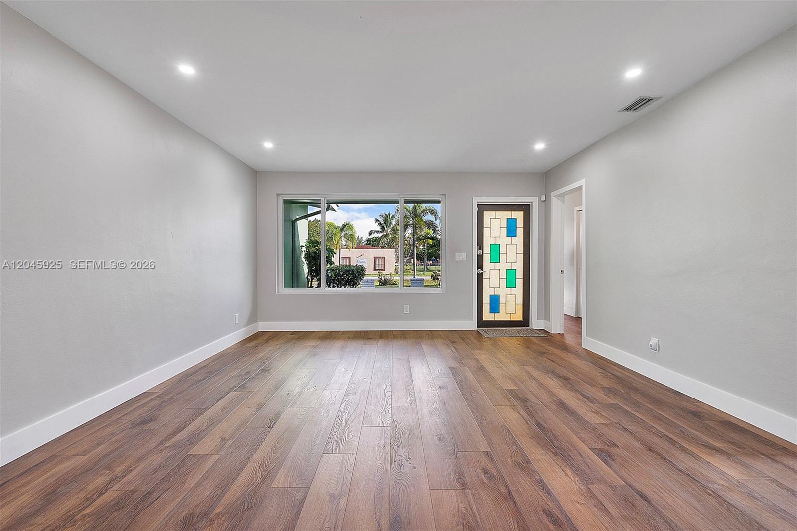 An empty living room features light gray walls, dark wood-look flooring, and a decorative glass door — 2230 Atlanta St, Hollywood FL 33020, HOLLYWOOD, FL