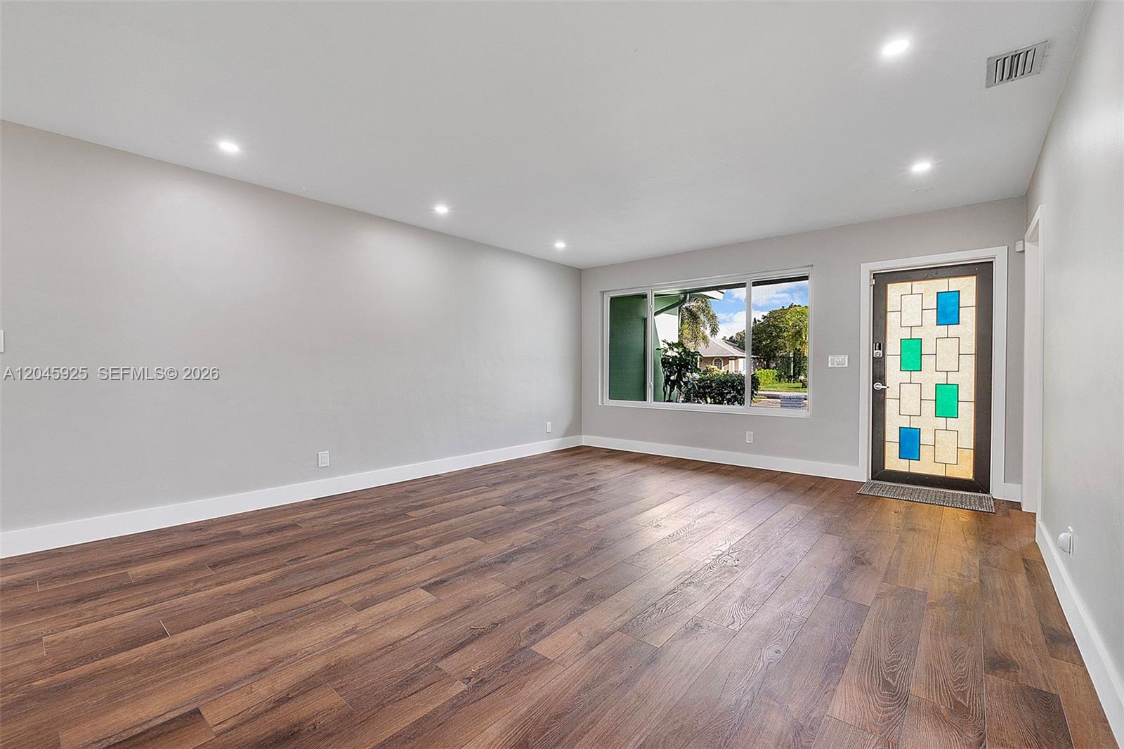 An empty room features wood-look flooring, recessed lighting, a large window, and a decorative door — 2230 Atlanta St, Hollywood FL 33020, HOLLYWOOD, FL