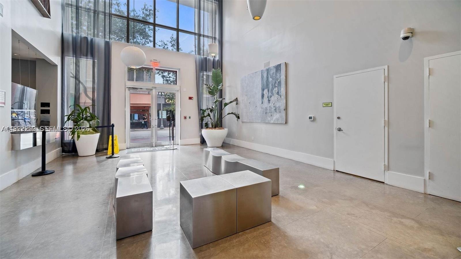 A modern lobby features high ceilings, floor-to-ceiling windows, metal bench seating, and tile flooring — 133 NE 2nd Ave # 2013, Miami FL 33132, MIAMI, FL
