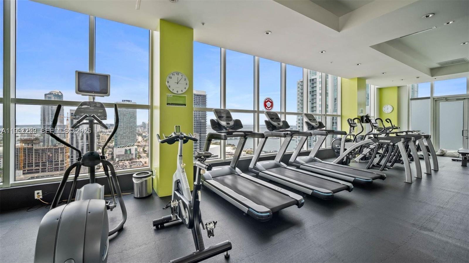 A gym features rows of treadmills and stationary bikes overlooking a city skyline and water — 133 NE 2nd Ave # 2013, Miami FL 33132, MIAMI, FL