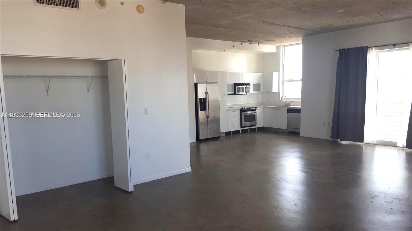 An open-concept kitchen with stainless steel appliances and concrete floors sits adjacent to a closet — 133 NE 2nd Ave # 2013, Miami FL 33132, MIAMI, FL