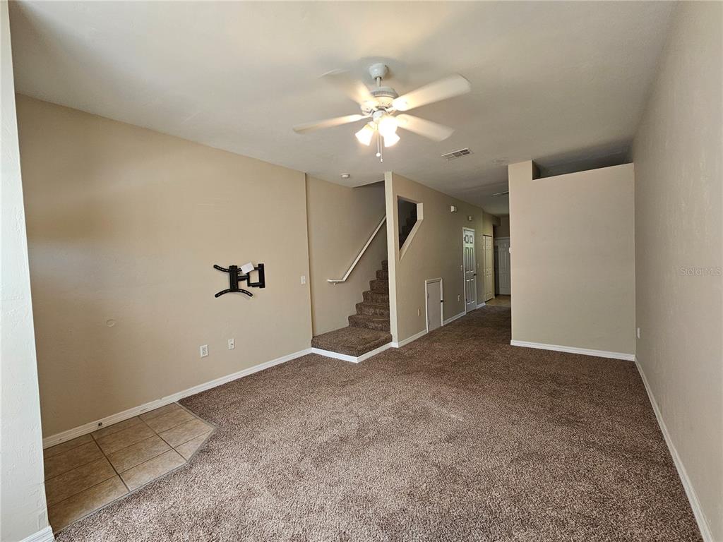An empty living room features beige walls, brown carpeting, a ceiling fan, and a staircase — 3575 SW 30TH WAY UNIT 118, GAINESVILLE, FL