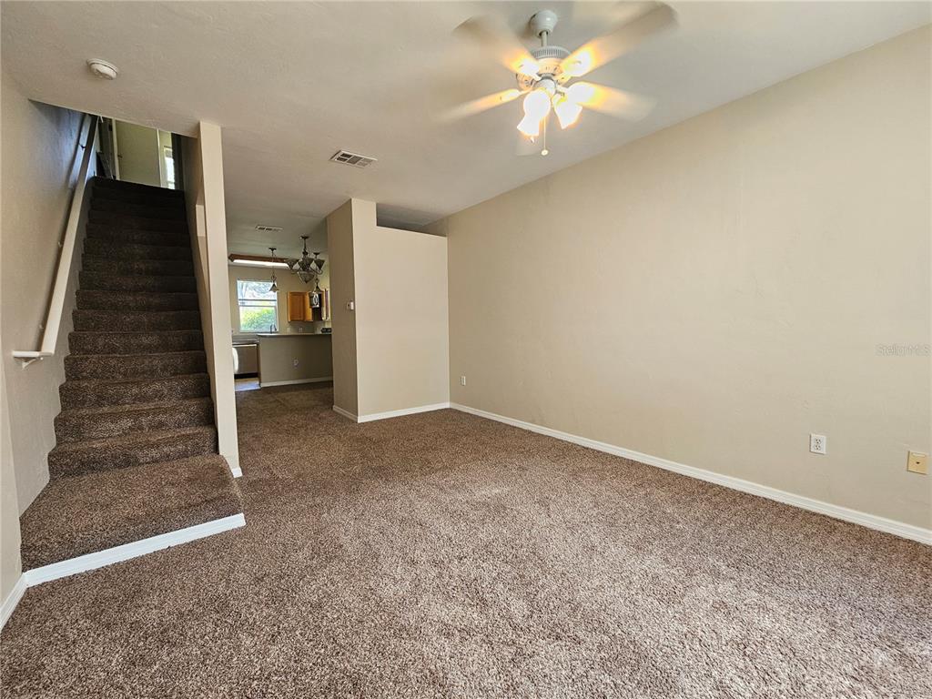 A carpeted living room features a staircase, a ceiling fan, and a view into the kitchen — 3575 SW 30TH WAY UNIT 118, GAINESVILLE, FL