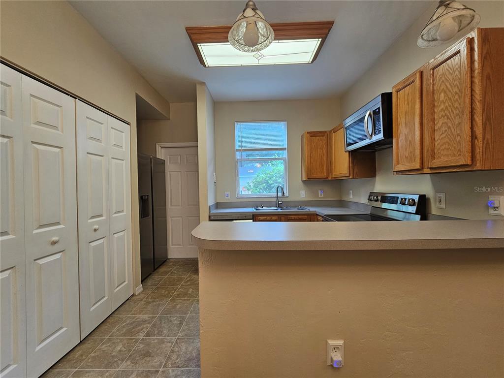 A kitchen features wood cabinets, a breakfast bar, tile flooring, and a stainless steel microwave — 3575 SW 30TH WAY UNIT 118, GAINESVILLE, FL