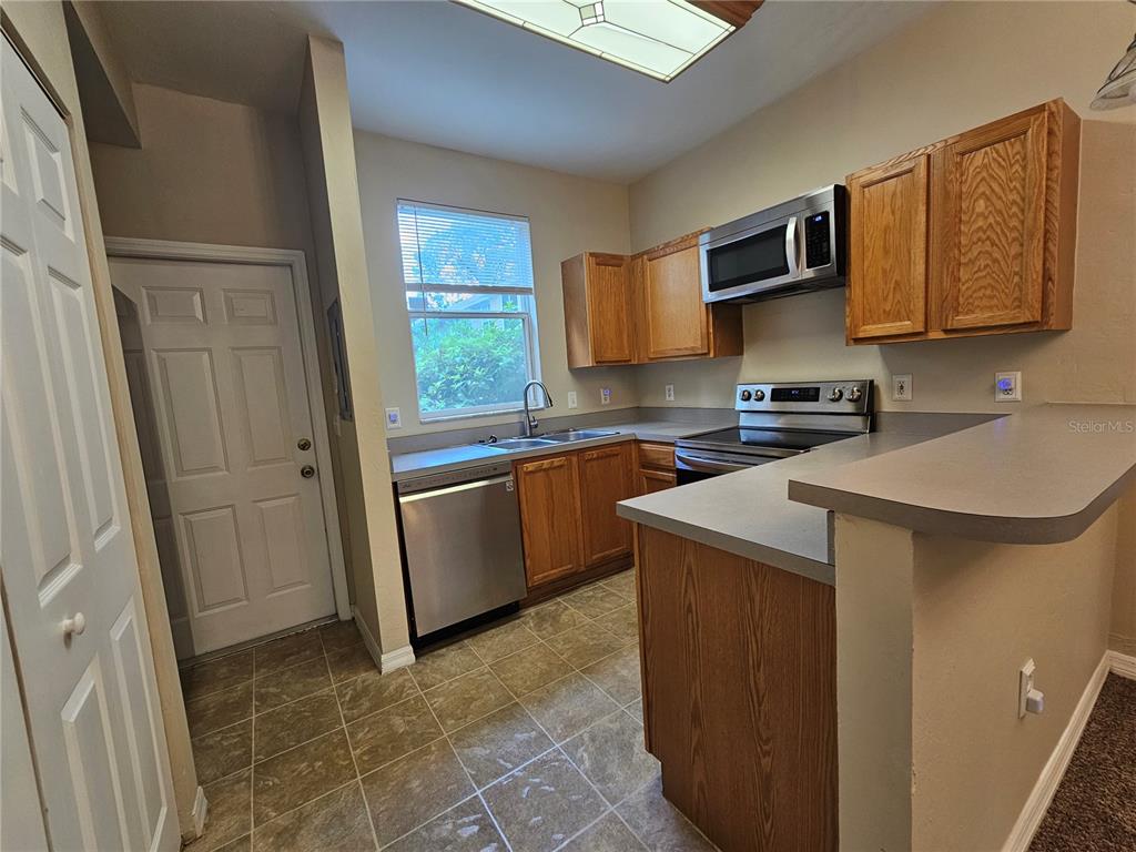 A kitchen features wood cabinets, gray countertops, stainless steel appliances, and tile flooring — 3575 SW 30TH WAY UNIT 118, GAINESVILLE, FL