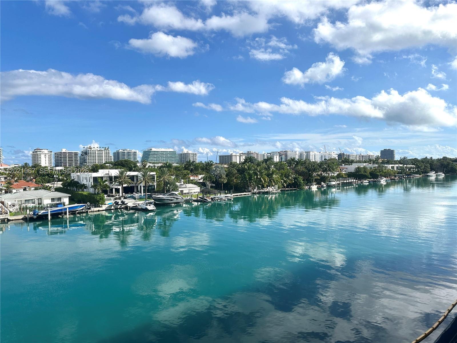 A view of a canal with docked boats, palm trees, and distant high-rise buildings — 9501 E Bay Harbor Dr # 5B, Bay Harbor Islands FL 33154, BAY HARBOR ISLANDS, FL