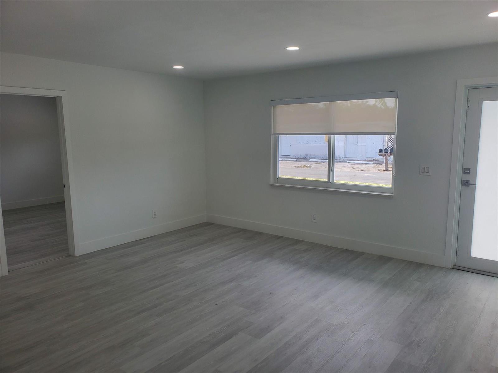 An empty room with white walls, light gray wood-look flooring, recessed lighting, and a window — 70 NW 13th Avenue # 2, Dania Beach FL 33004, DANIA BEACH, FL