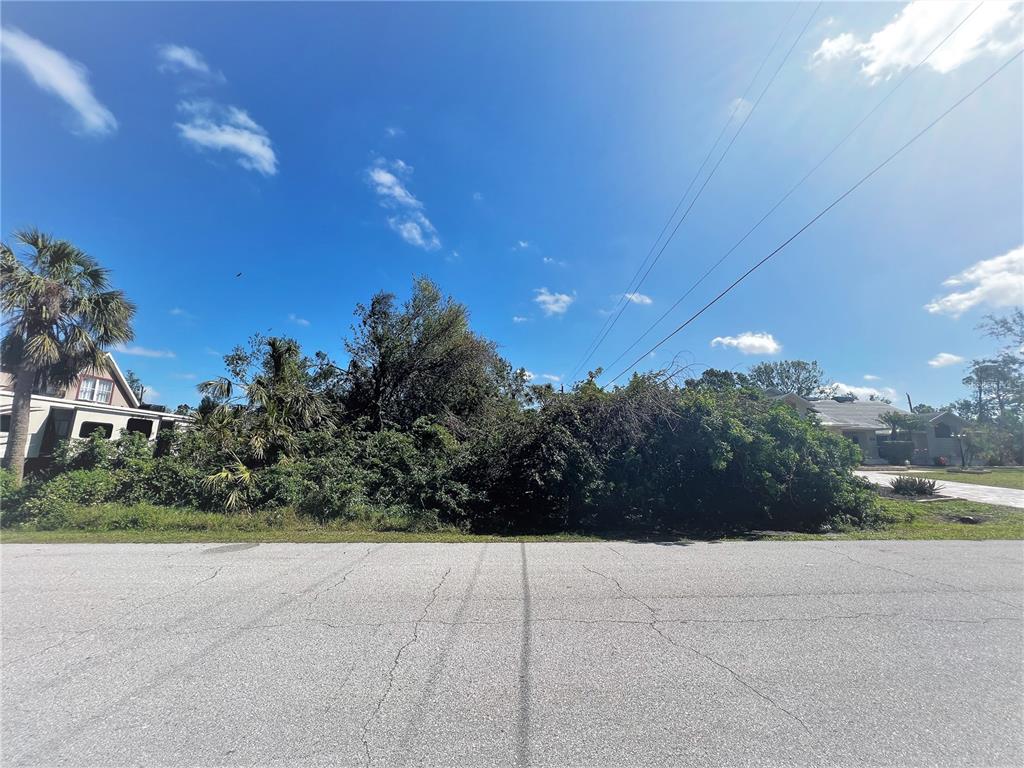 A vacant, overgrown residential lot sits between two houses along a paved street — 3438 DUNKIRK STREET, PORT CHARLOTTE, FL