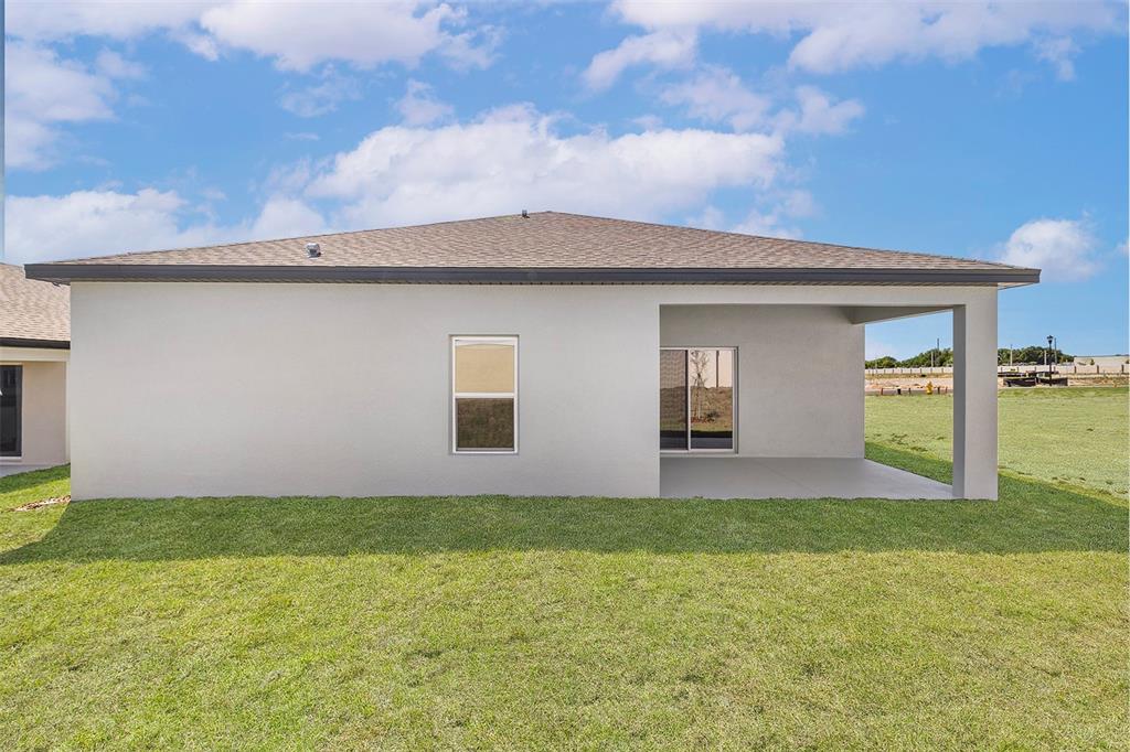 The exterior rear view of a house shows a covered patio and a grassy yard — 1802 WHITE ELEPHANT LOOP, WINTER HAVEN, FL