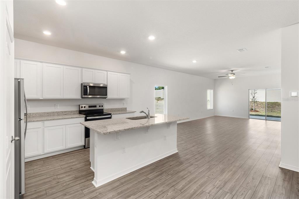 A modern kitchen with white cabinets, granite countertops, and an island opens into a living area — 1802 WHITE ELEPHANT LOOP, WINTER HAVEN, FL