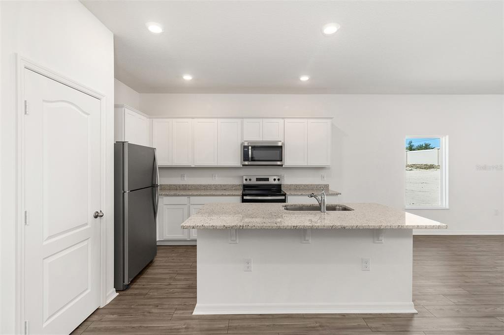 A modern kitchen features white cabinetry, granite countertops, stainless steel appliances, and a central island — 1802 WHITE ELEPHANT LOOP, WINTER HAVEN, FL