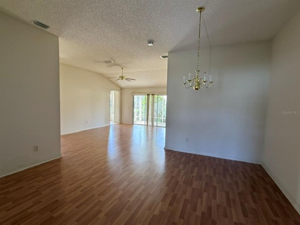 An open-concept living and dining area features wood-look flooring, a chandelier, and sliding glass doors — 3001 SAINT THOMAS LANE, THE VILLAGES, FL