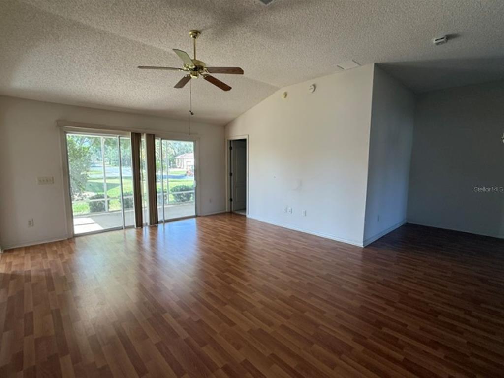A spacious living room features wood-look laminate flooring, a vaulted ceiling, and sliding glass doors — 3001 SAINT THOMAS LANE, THE VILLAGES, FL