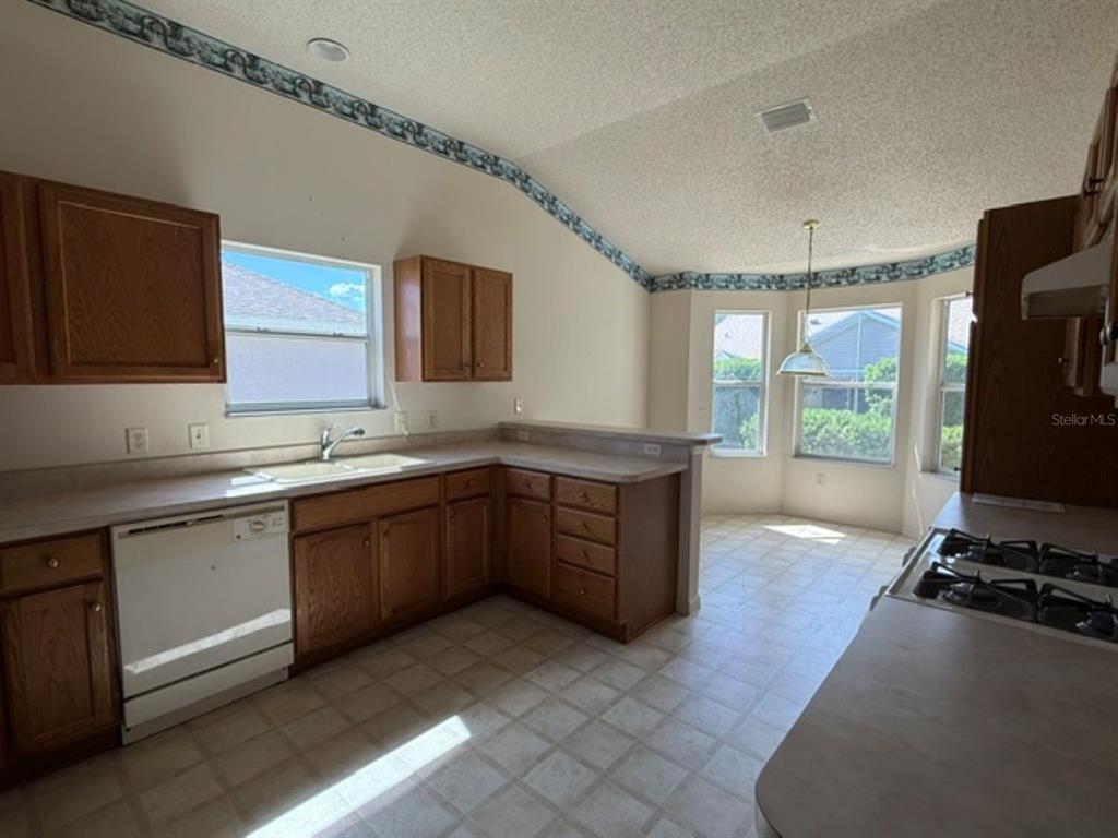 A kitchen with wood cabinets, laminate countertops, a white dishwasher, and a breakfast nook area — 3001 SAINT THOMAS LANE, THE VILLAGES, FL
