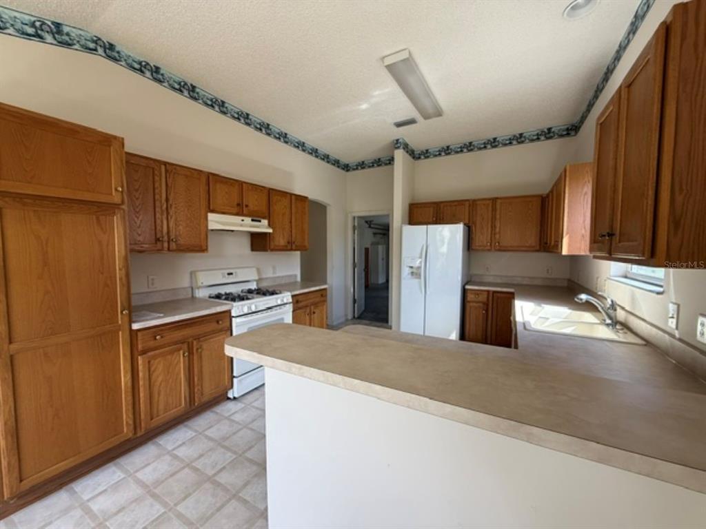 A kitchen features oak cabinets, laminate countertops, white appliances, and a patterned wallpaper border — 3001 SAINT THOMAS LANE, THE VILLAGES, FL