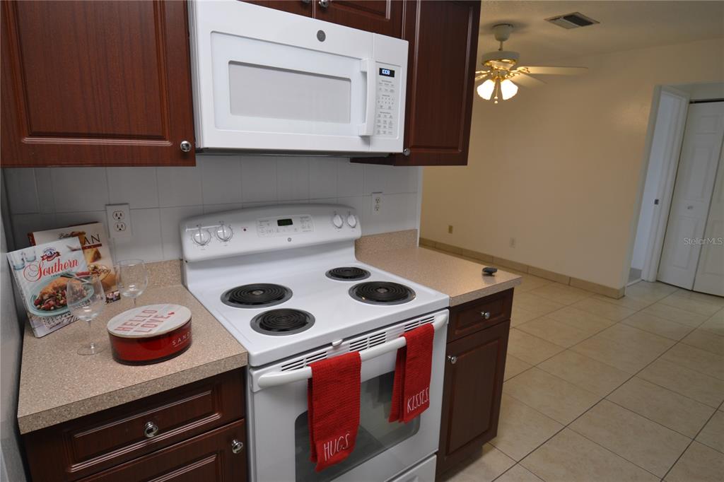 A kitchen features dark wood cabinets, a white stove, a microwave, and beige countertops — 2357 WHITE OAK CIRCLE, CLEARWATER, FL