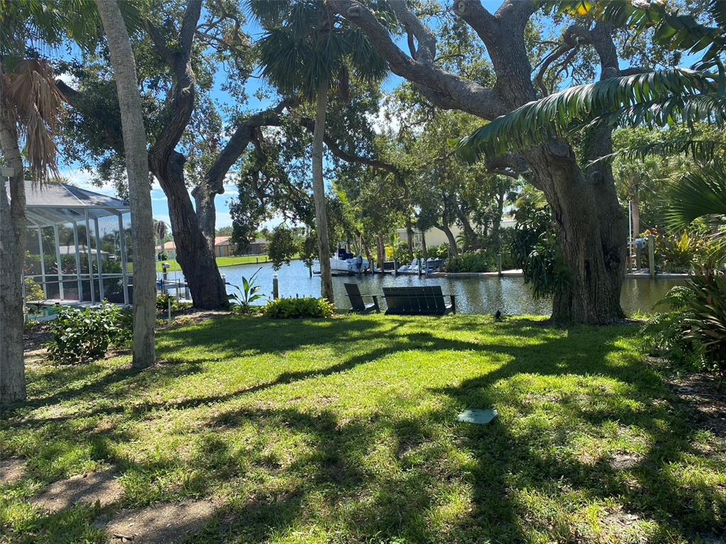 A grassy backyard features large oak trees, a canal view, and a small seating area — 814 PARADISE WAY, SARASOTA, FL