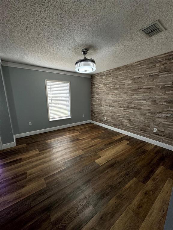 An empty room features wood-look flooring, a stone accent wall, and a modern ceiling fan — 604 TAMARIN LANE, KISSIMMEE, FL