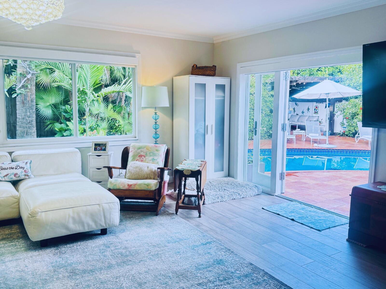 A living room with a white sofa, floral armchair, and glass doors opening to a pool — 3209 Norfolk Street, Pompano Beach FL 33062, POMPANO BEACH, FL