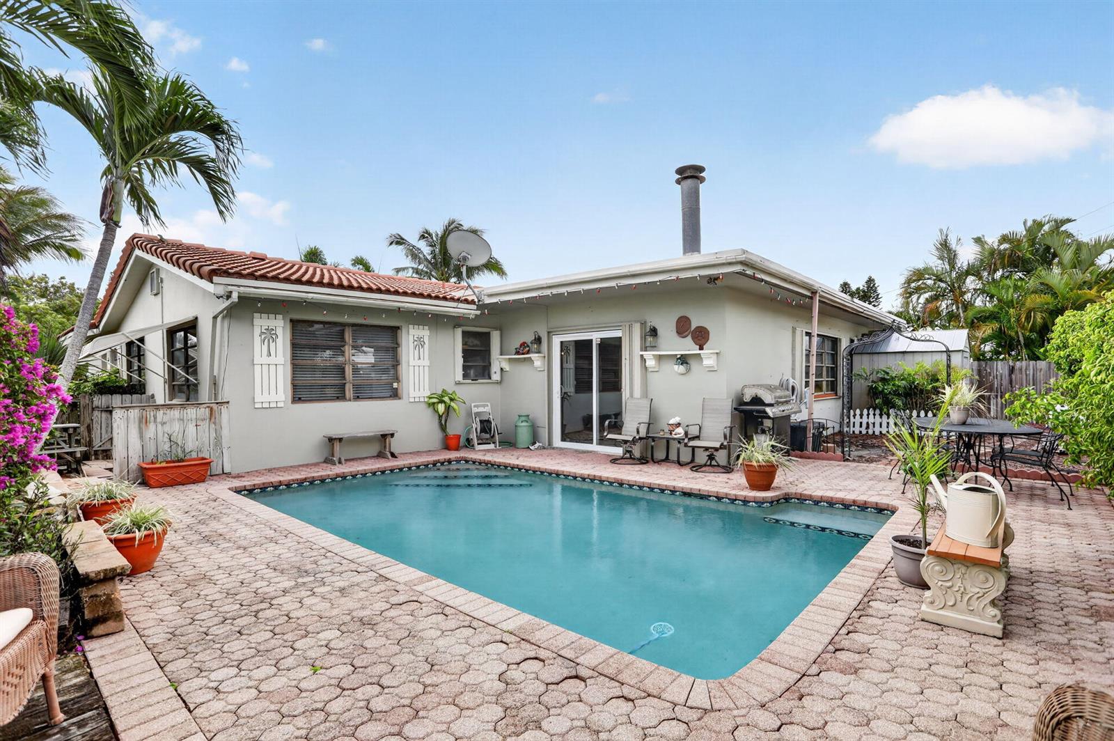 A backyard swimming pool sits on a paved patio next to a single-story house — 1931 NE 27th Street, Lighthouse Point FL 33064, LIGHTHOUSE POINT, FL