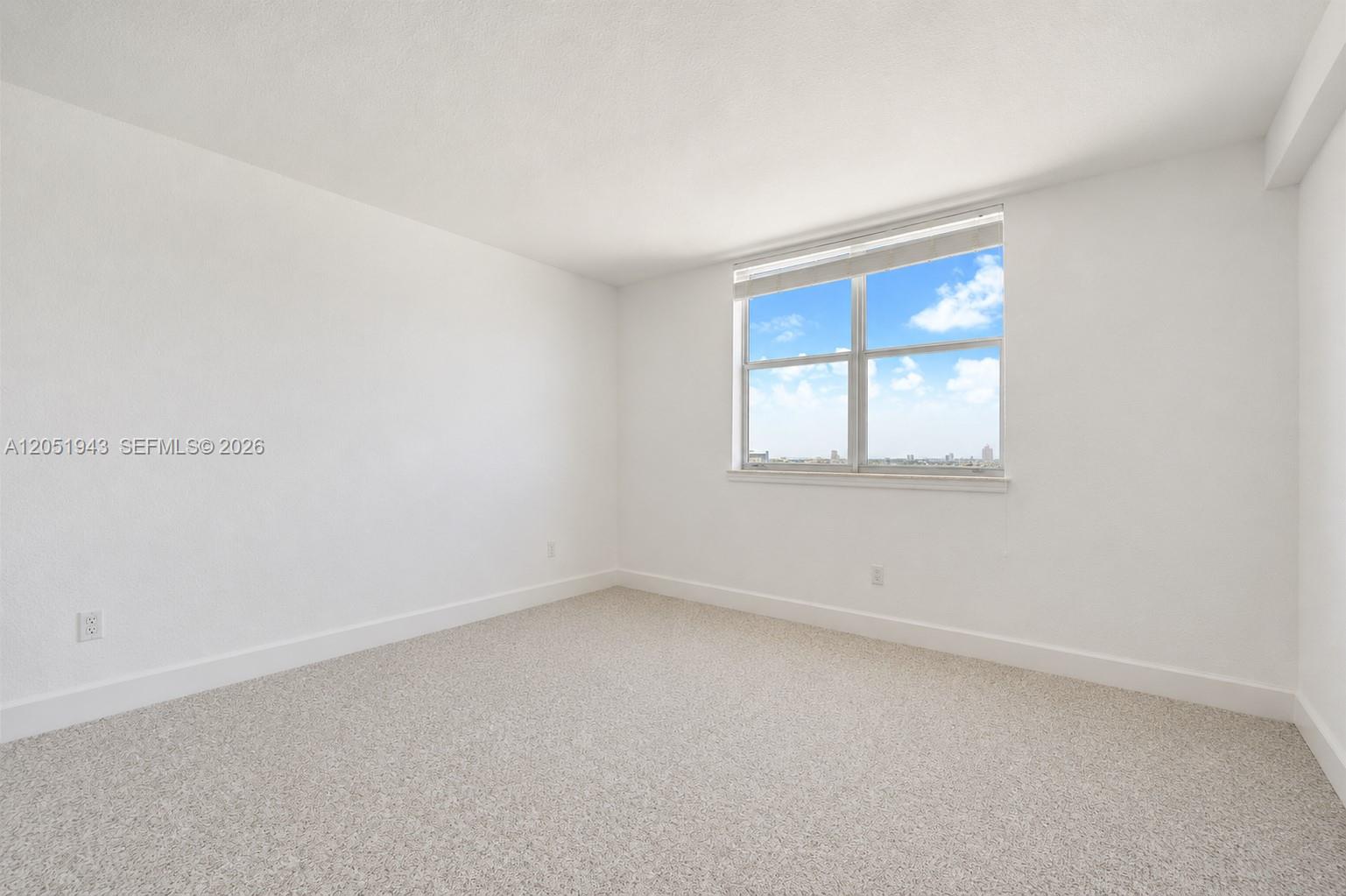 An empty bedroom features white walls, beige carpeting, and a window with a city view — 401 69th St # 1411, Miami Beach FL 33141, MIAMI BEACH, FL