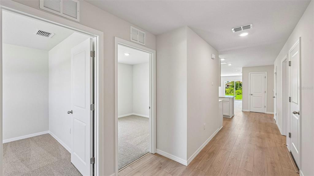 A hallway with light wood-look flooring leads toward a kitchen with white cabinets and appliances — 12318 HOPSCOTCH AVENUE, PARRISH, FL