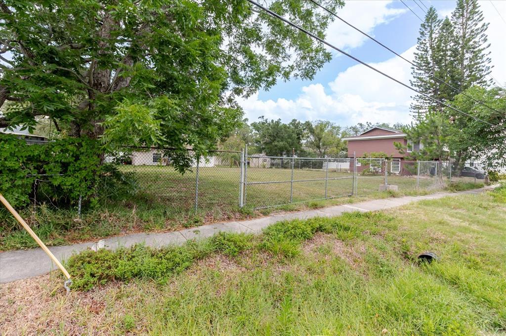 A fenced, grassy vacant lot sits next to a sidewalk and a two-story house — 7208 S SHERRILL, TAMPA, FL