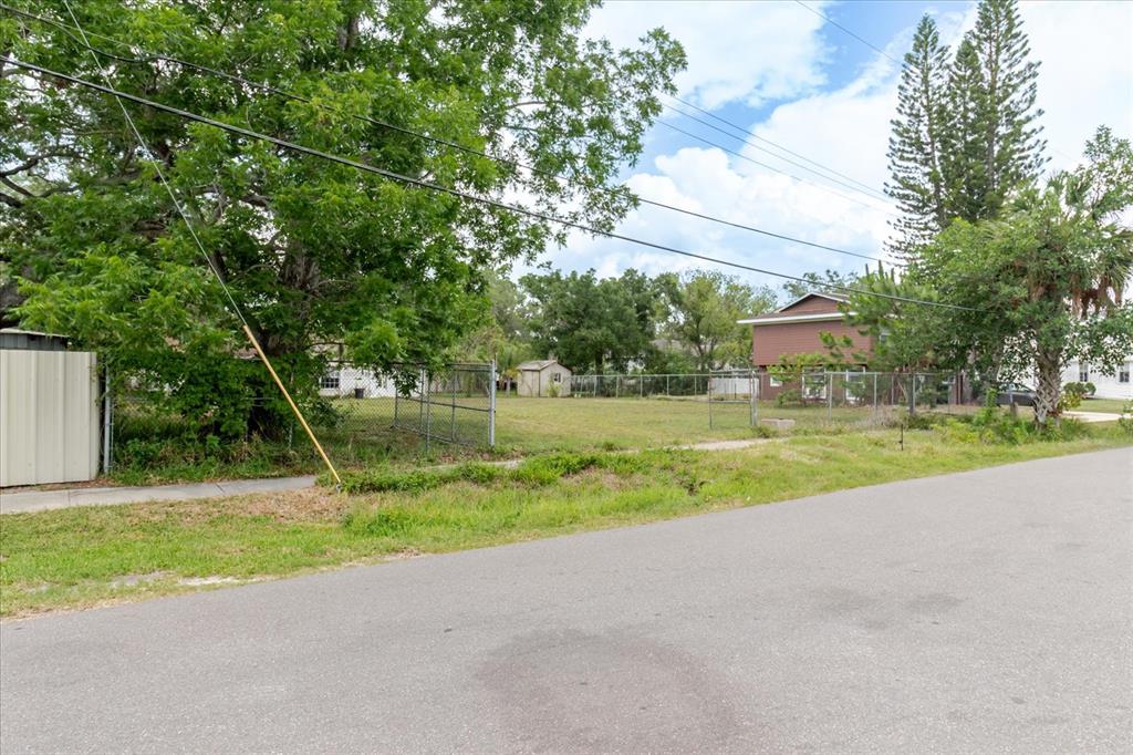 A vacant, fenced-in residential lot sits beside a paved street with trees and nearby houses — 7208 S SHERRILL, TAMPA, FL