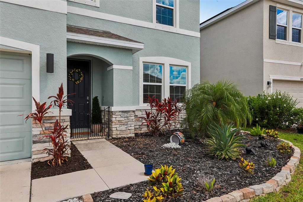 The exterior of a two-story house features light blue stucco, stone accents, and a landscaped yard — 16976 OVAL RUM DRIVE, WIMAUMA, FL