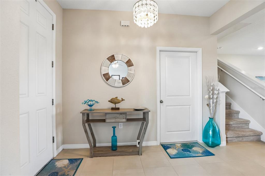 A bright entryway features a console table, a round mirror, and stairs leading upward — 16976 OVAL RUM DRIVE, WIMAUMA, FL