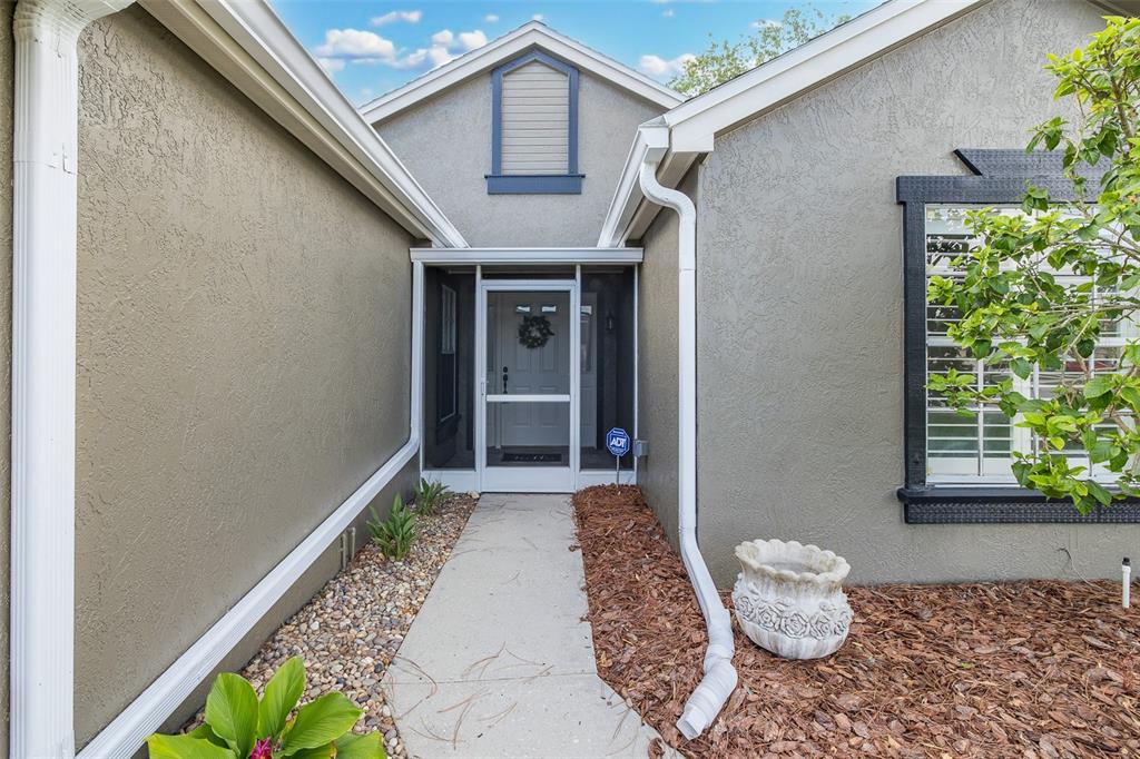 A concrete walkway leads to a screened front door of a house with stucco siding — 4242 NORTHAMPTON DRIVE, NEW PORT RICHEY, FL