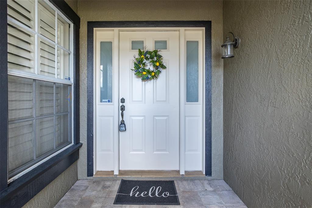 A white front door with a lemon wreath and a hello doormat under a porch light — 4242 NORTHAMPTON DRIVE, NEW PORT RICHEY, FL