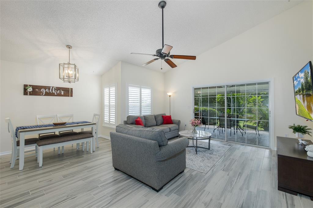 A living and dining area with gray tile floors, a ceiling fan, and sliding glass doors — 4242 NORTHAMPTON DRIVE, NEW PORT RICHEY, FL
