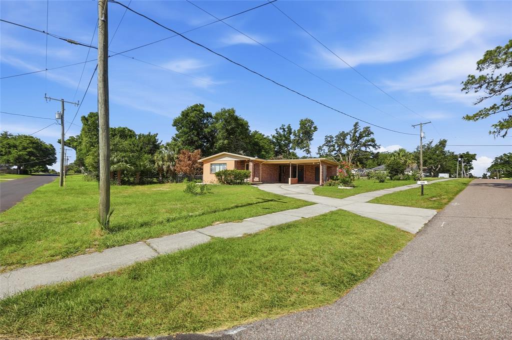A single-story house with a brick facade and attached carport sits on a grassy corner lot — 620 W CUMMINGS STREET, LAKE ALFRED, FL