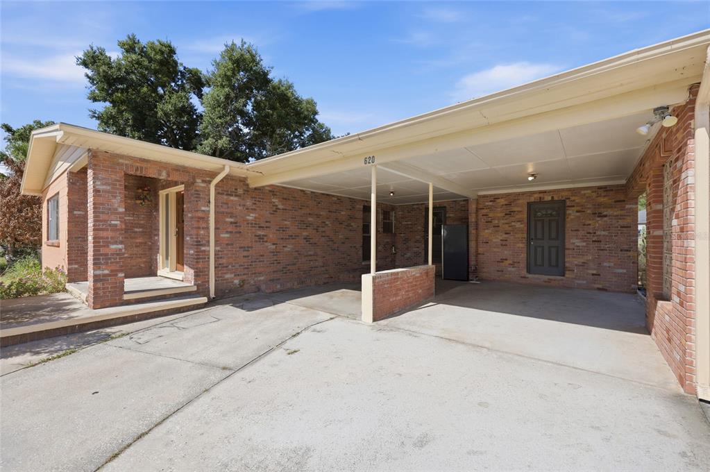 A brick house exterior features a concrete driveway leading to a covered carport and entrance — 620 W CUMMINGS STREET, LAKE ALFRED, FL