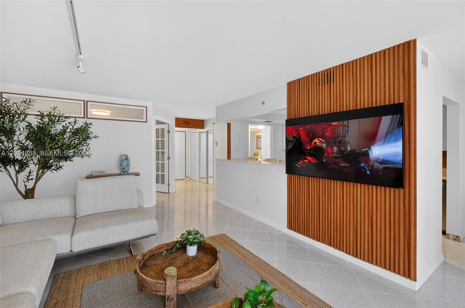 A living room features a slatted wood accent wall with a mounted television and tile flooring — 2401 Collins Ave # 1406, Miami Beach FL 33140, MIAMI BEACH, FL