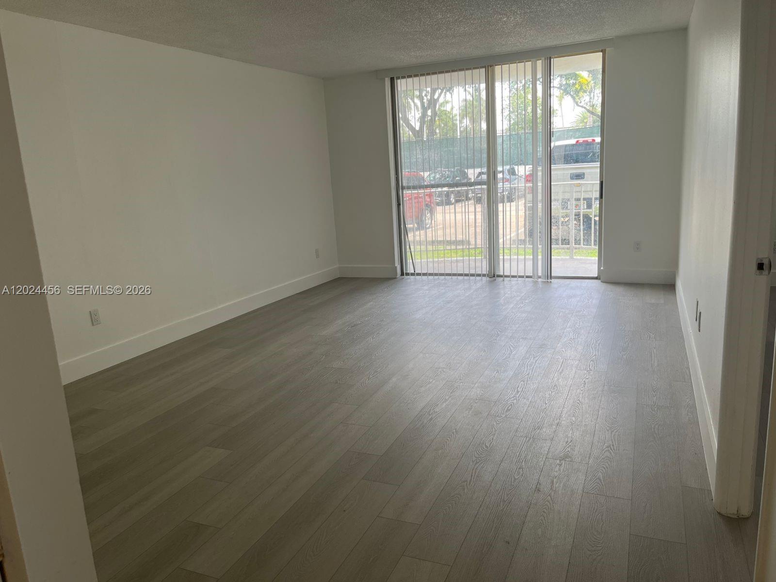 An empty room features light gray wood-look flooring, white walls, and a kitchen pass-through window — 484 NW 165th St Rd # 111, Miami FL 33169, MIAMI, FL