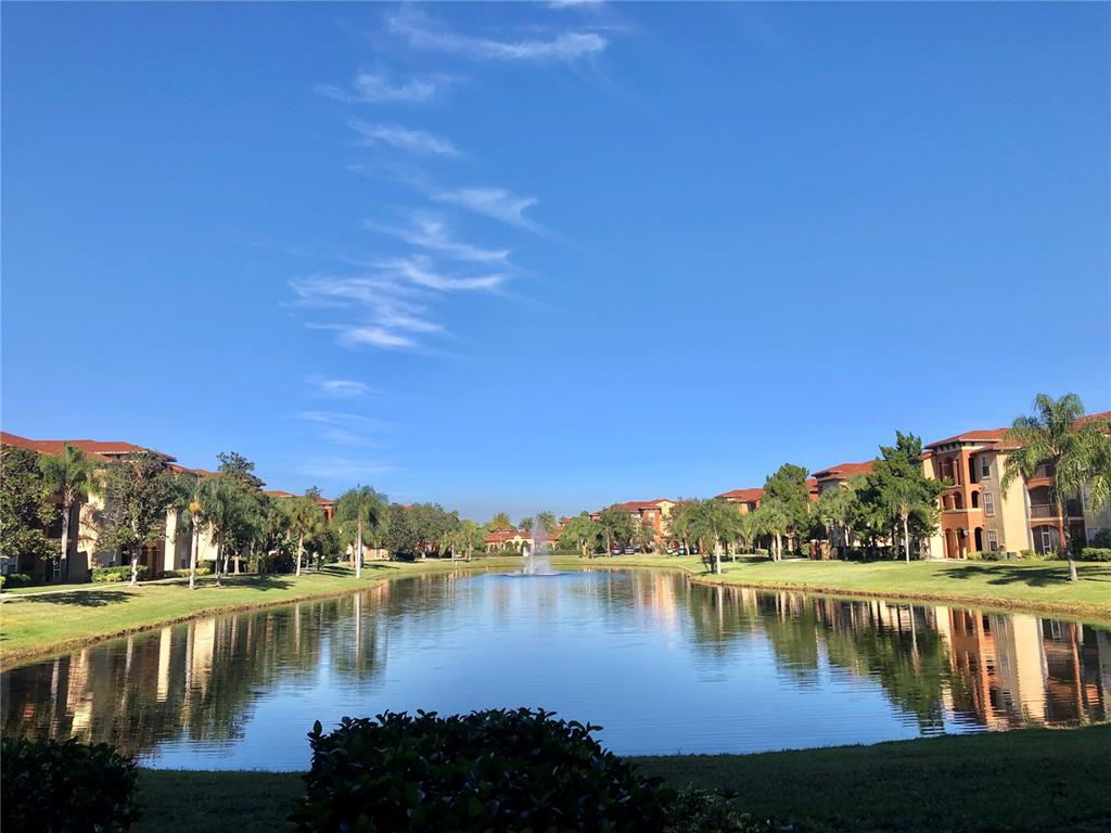 A pond with a fountain sits between two apartment buildings under a blue sky — 5542 METROWEST BOULEVARD UNIT 104, ORLANDO, FL