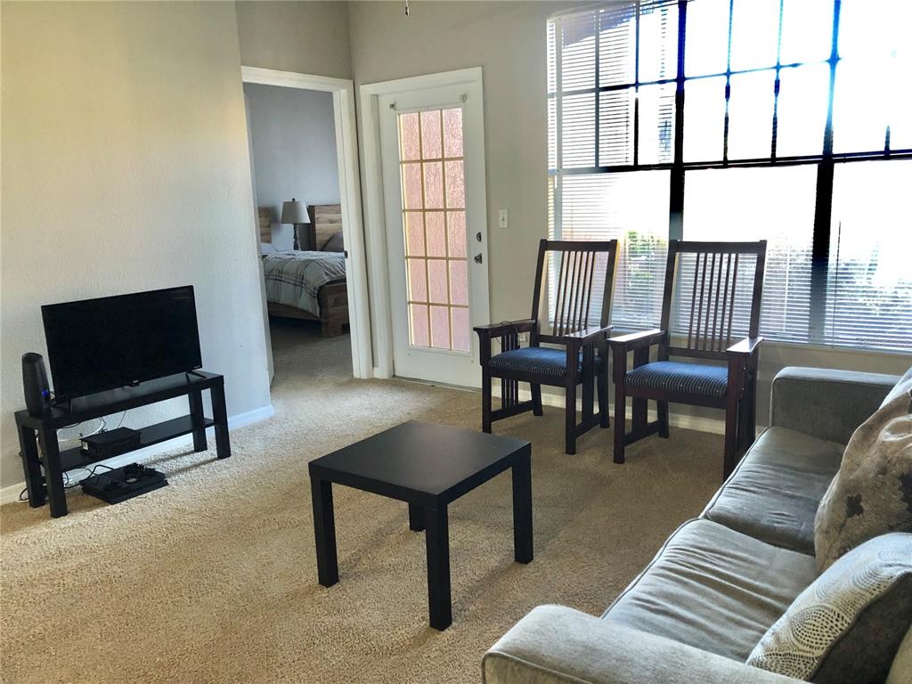 A living room features a television, coffee table, two wooden chairs, and a sofa — 5542 METROWEST BOULEVARD UNIT 104, ORLANDO, FL