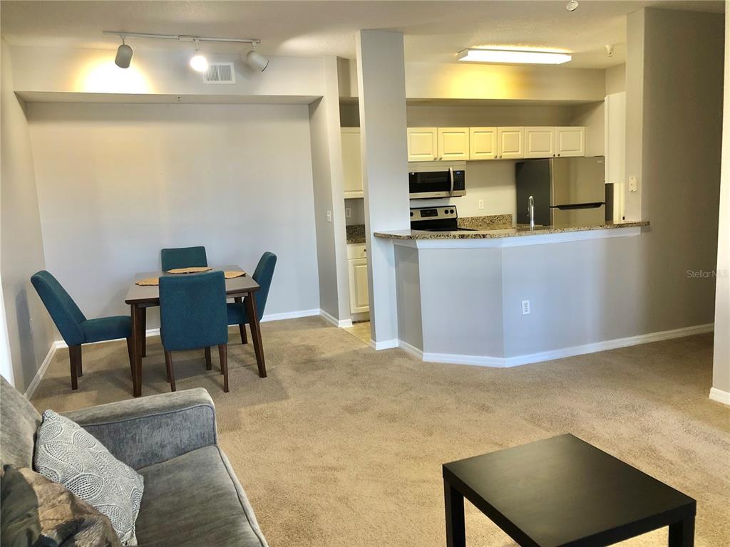 A dining area with blue chairs sits next to a kitchen with a breakfast bar — 5542 METROWEST BOULEVARD UNIT 104, ORLANDO, FL