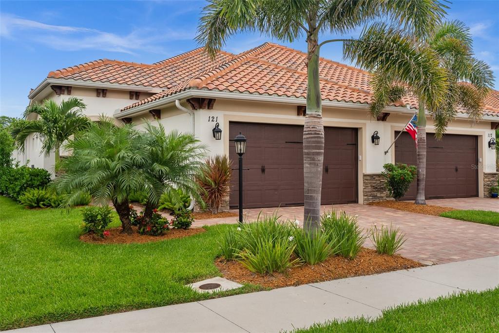 A single-story house with a tiled roof, two garage doors, and palm trees in front — 121 COLEBROOK COURT, VENICE, FL