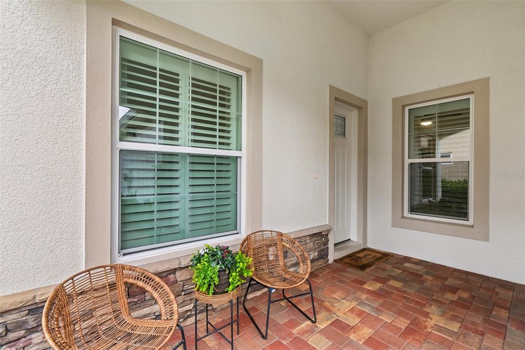 A covered patio features a brick paver floor, stone siding, two wicker chairs, and windows — 121 COLEBROOK COURT, VENICE, FL