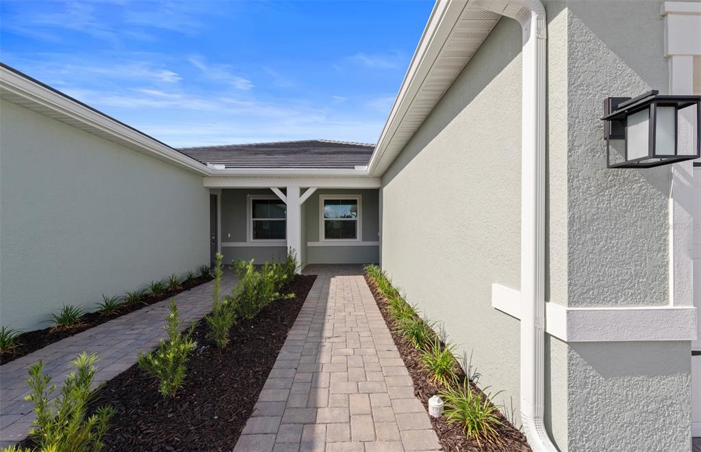 A paved walkway leads to the front entrance of a house with light-colored stucco walls — 1603 TAVIRA PLACE, ENGLEWOOD, FL