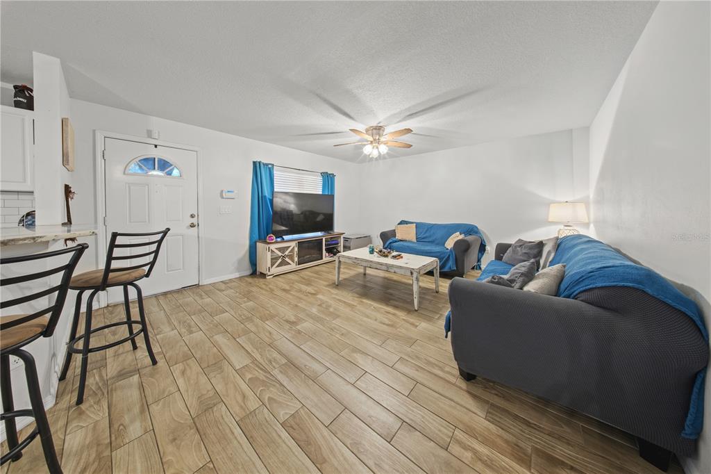 A living room features wood-look tile flooring, a ceiling fan, and two blue-covered sofas — 1806 E CURTIS STREET, TAMPA, FL