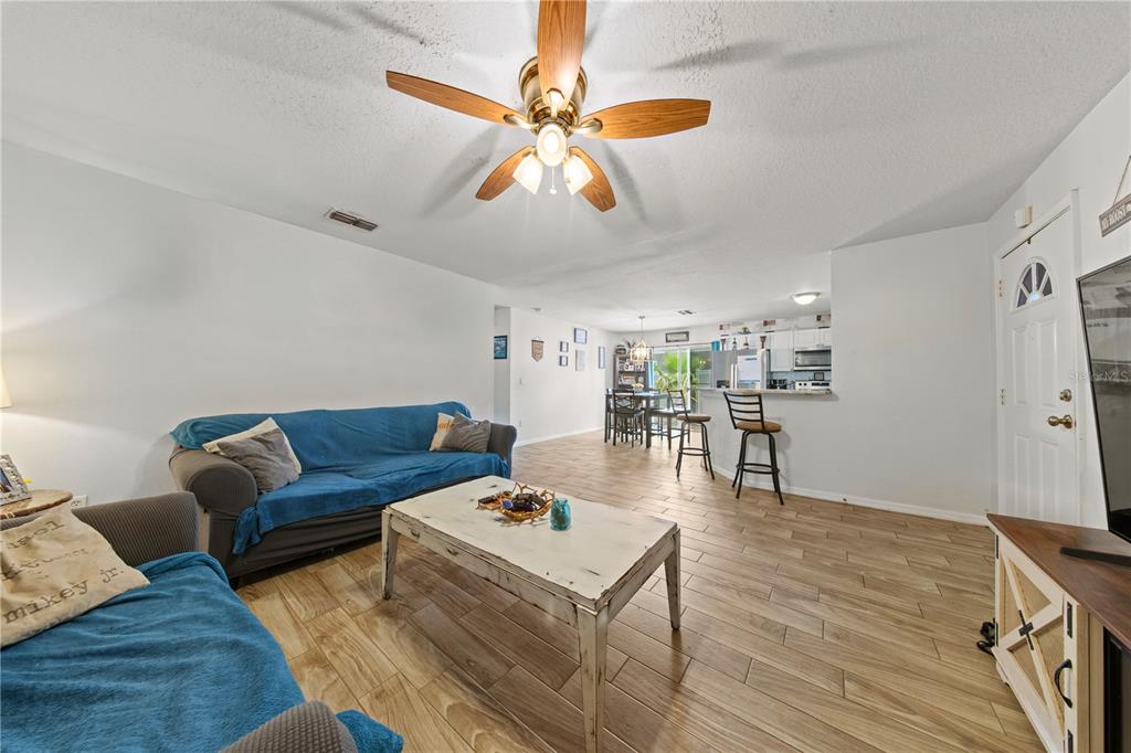 A living room with wood-look tile flooring, a blue sofa, and an open kitchen area — 1806 E CURTIS STREET, TAMPA, FL