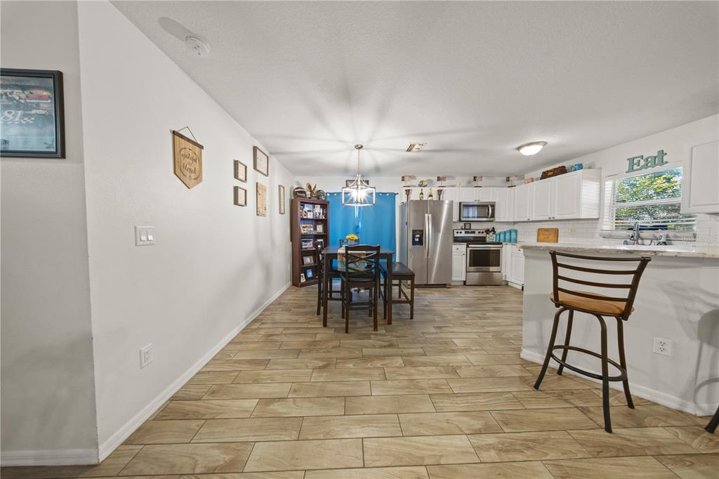 An open-concept kitchen and dining area features white cabinets, stainless steel appliances, and wood-look flooring — 1806 E CURTIS STREET, TAMPA, FL