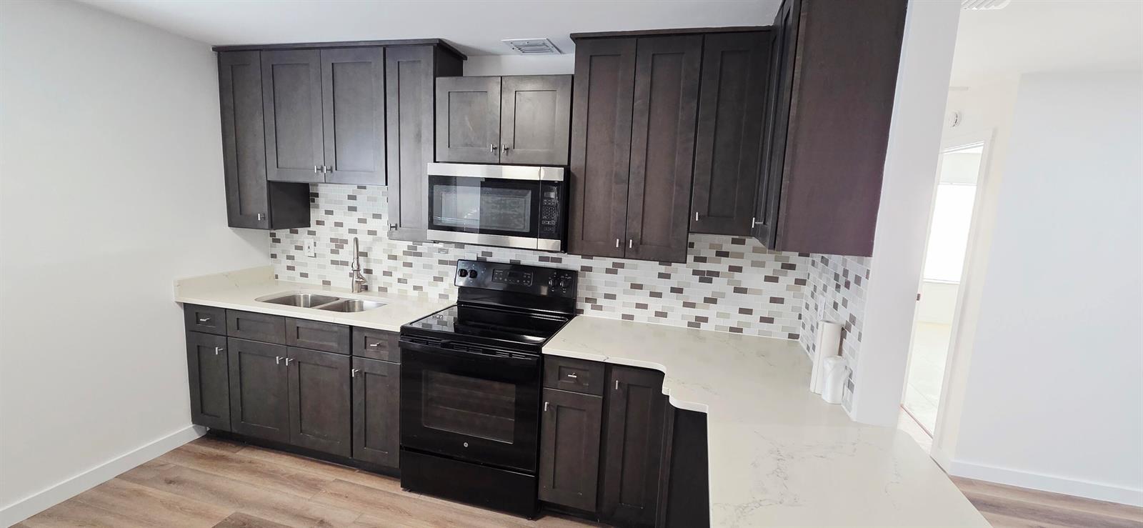 A kitchen features dark wood cabinets, a black stove, a microwave, and a tiled backsplash — 765 W 7th Street # B, Riviera Beach FL 33404, RIVIERA BEACH, FL
