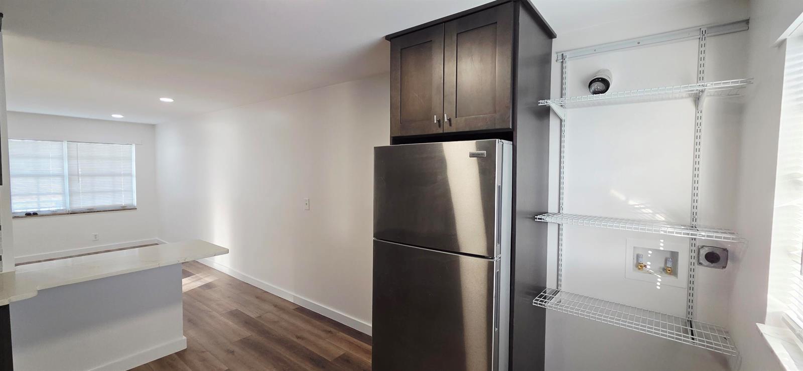 A stainless steel refrigerator stands next to white wire shelving and laundry hookups in a kitchen — 765 W 7th Street # B, Riviera Beach FL 33404, RIVIERA BEACH, FL